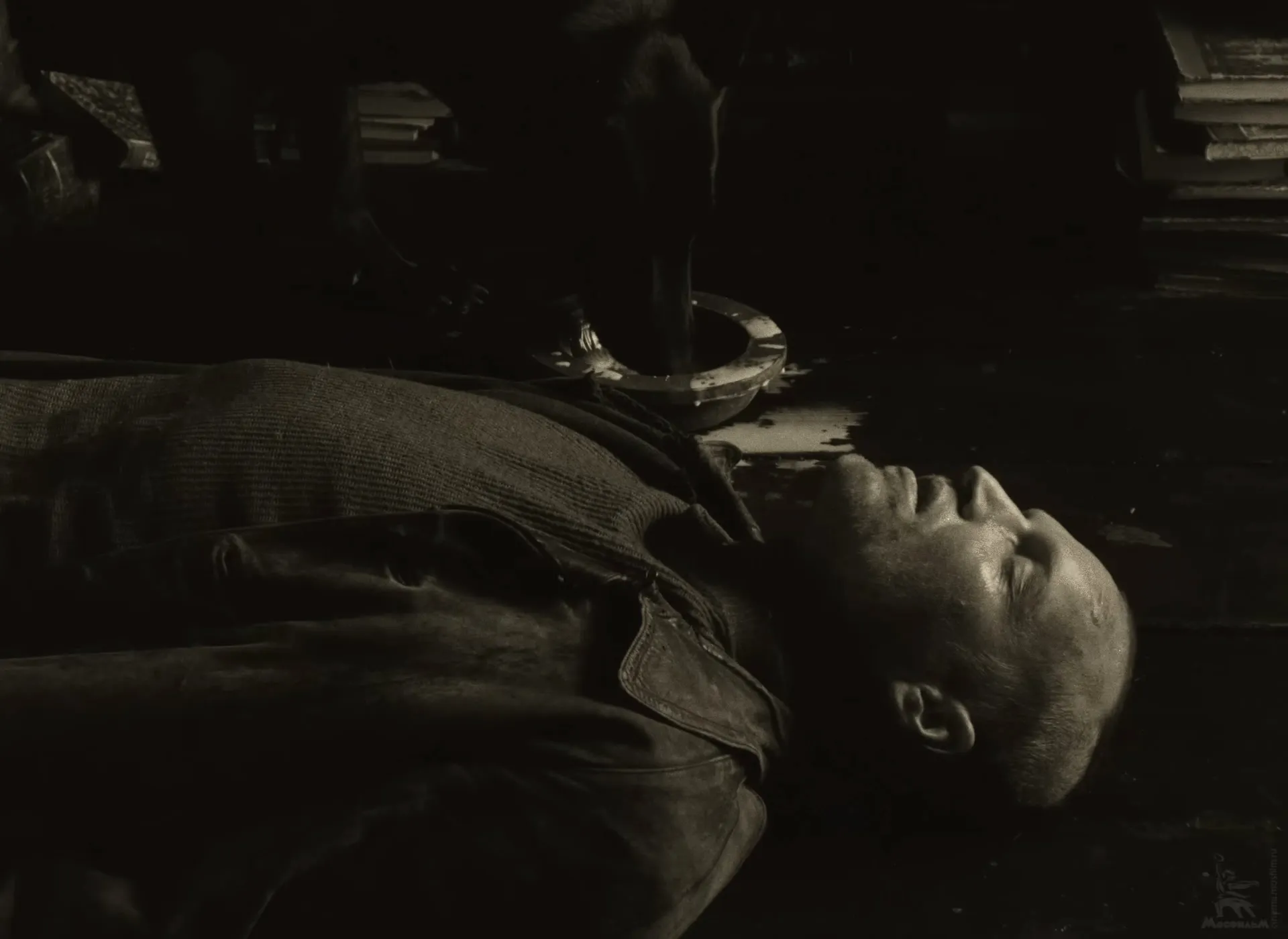 The black dog drinking milk from a bowl on the floor of the Stalker’s home, the Stalker lying on his back beside it.