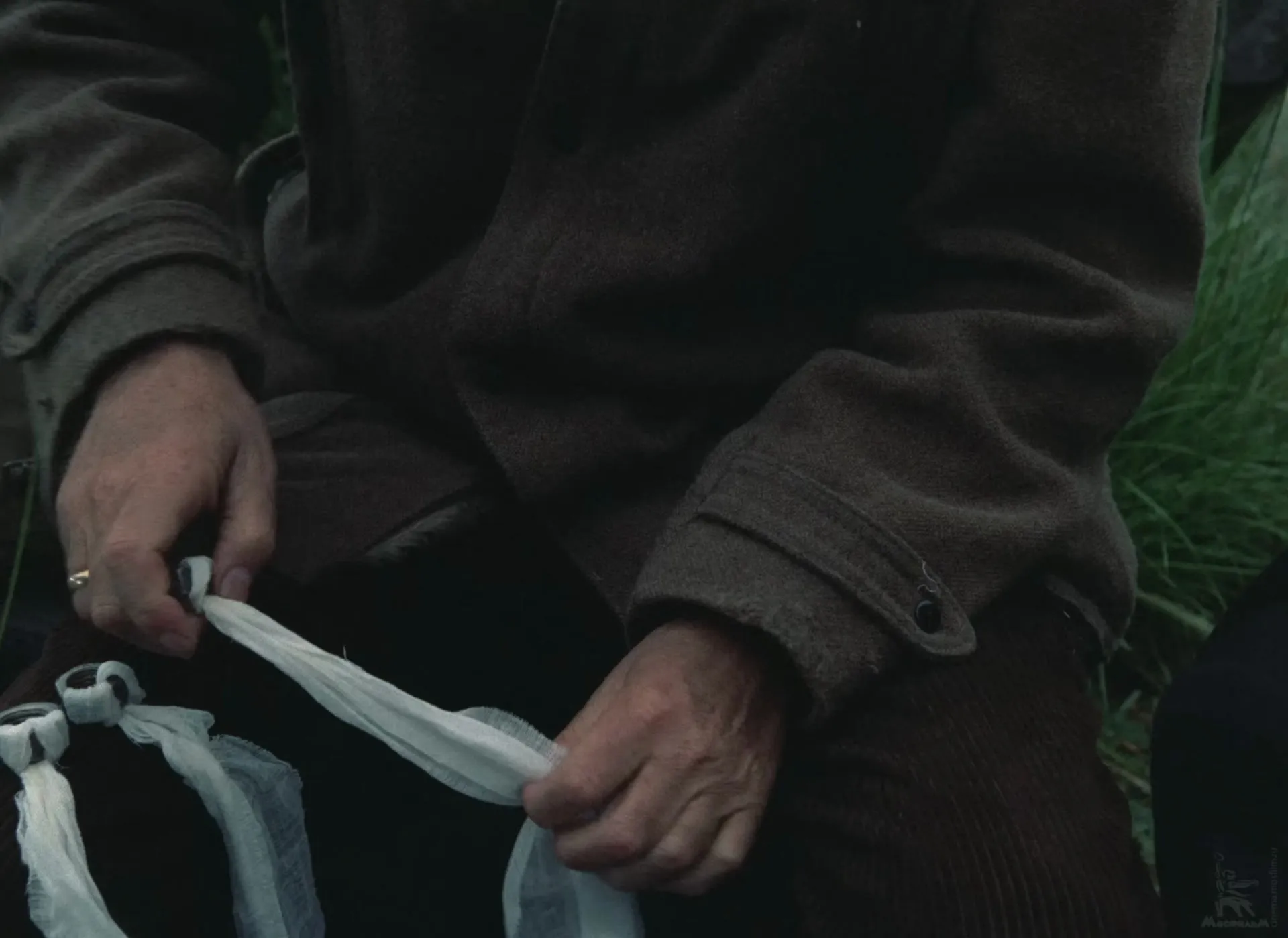 The Professor’s hands threading a strip of white bandage through a metal nut, finished ones beside him.