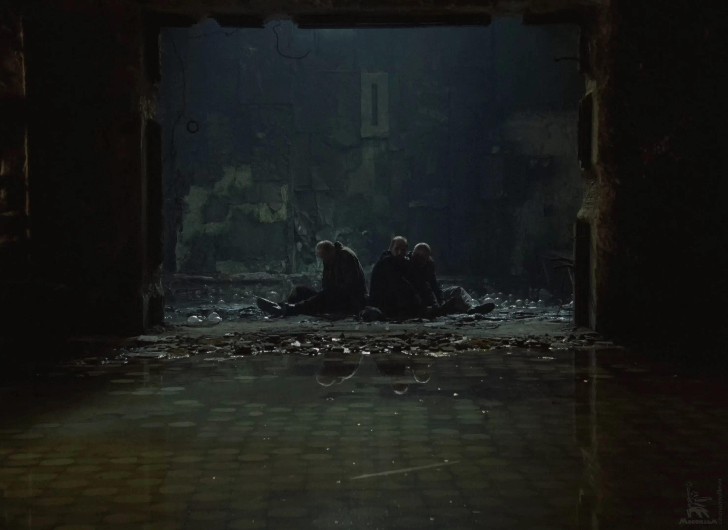The three men sit side by side in the doorway of the Room, seen from inside it.