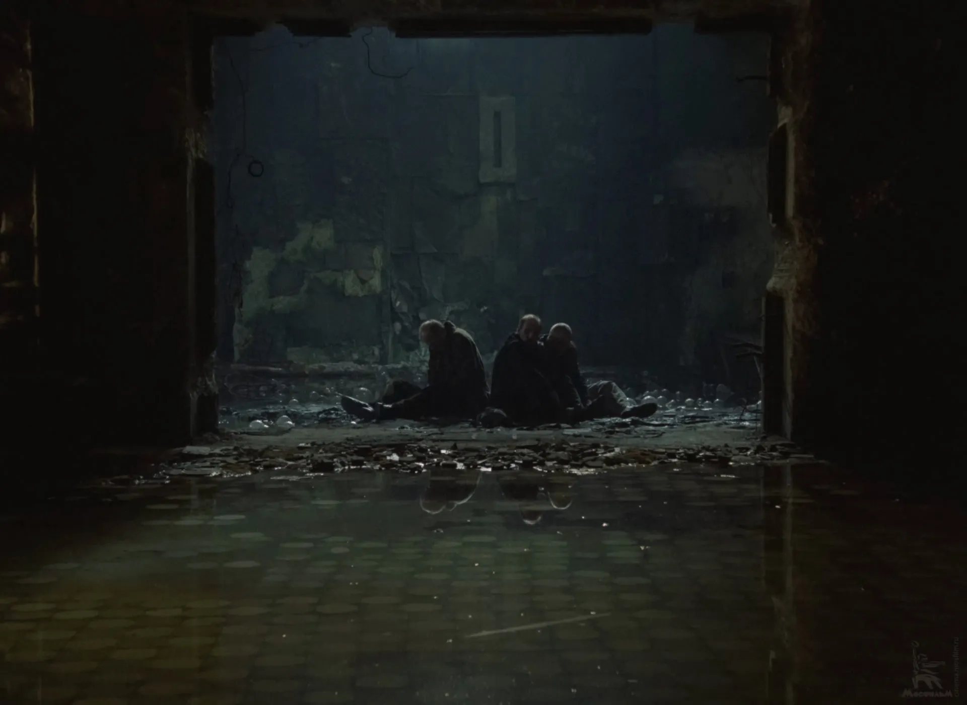 The three men sitting side by side in the Room’s doorway, seen from inside the Room.