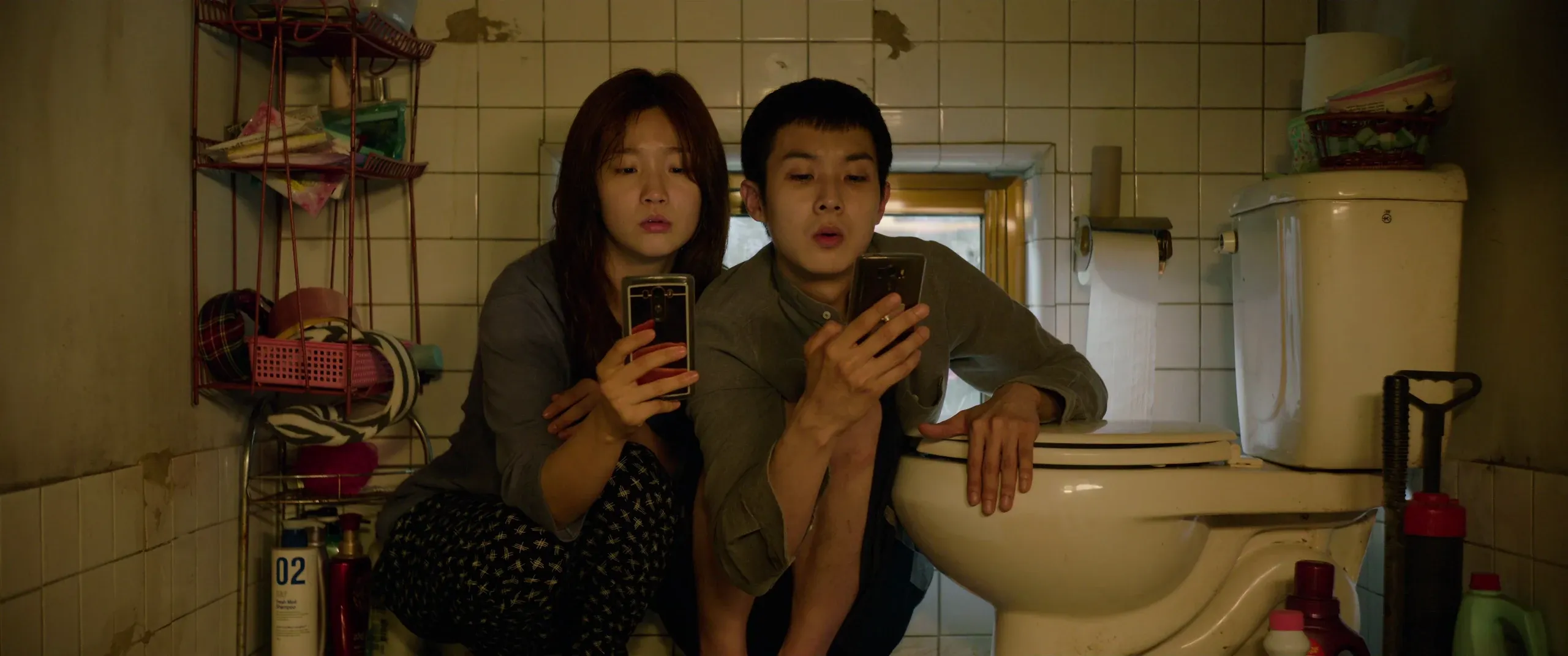 Ki-woo and Ki-jung crouched by the raised toilet, phones held up for a signal