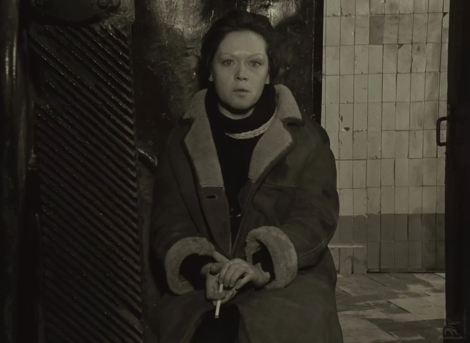 The Stalker’s wife sitting by the open door with a cigarette, looking straight into the camera.
