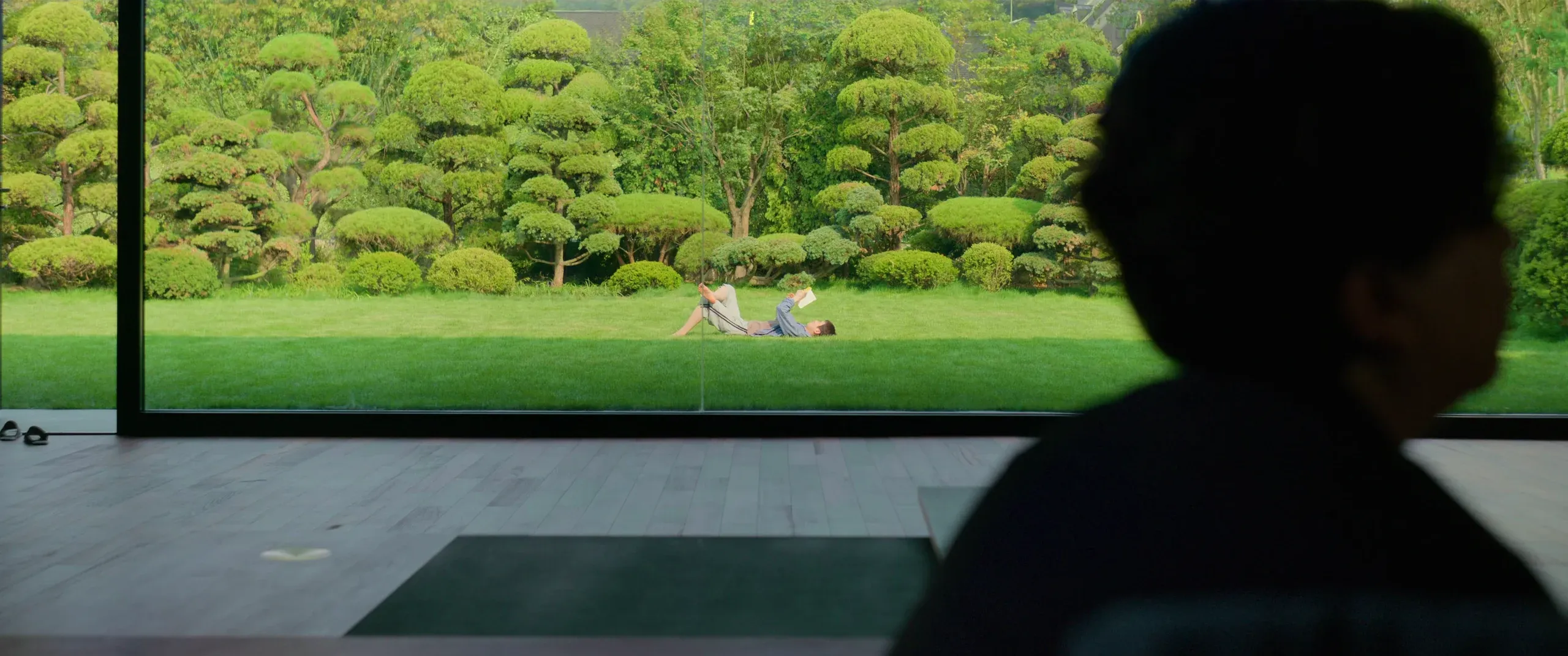 The Parks’ glass wall frames the sunlit garden, with Chung-sook silhouetted inside.